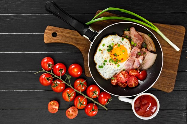 Uova fritte con prosciutto in padella su fondo di legno nero Vista dall'alto