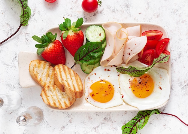 Uova fritte con prosciutto pomodori cetriolo fragole e toast Deliziosa colazione inglese Brunch Vista dall'alto