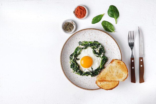 Uova fritte con spinaci freschi e crema di formaggio su un piatto om sfondo bianco vista dall'alto copia spazio