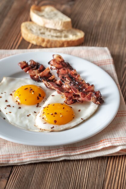 Uova fritte e pancetta affumicata sul piatto bianco