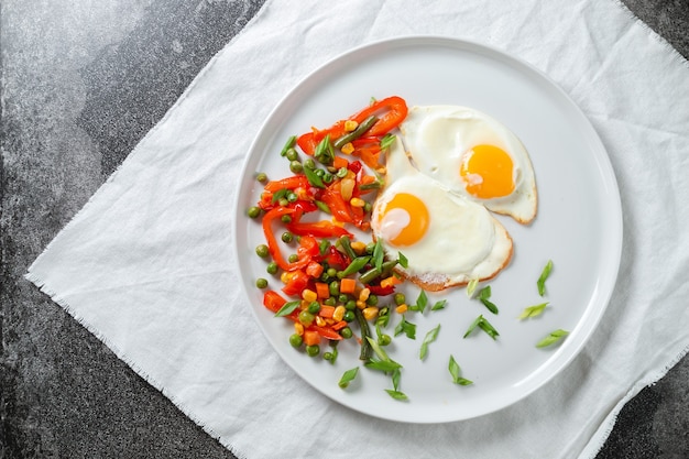 Uova fritte e verdure su un piatto bianco su un tavolo coperto con una tovaglia bianca