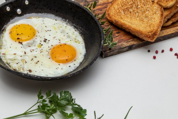 Uova fritte in un tegame di ferro rustico, pane tostato su un piatto per colazione.