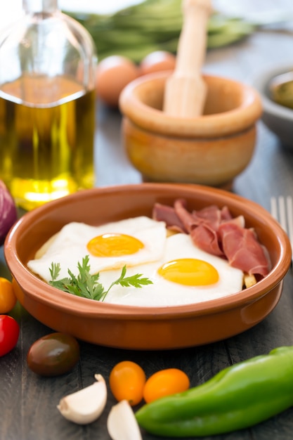 Uova fritte in una tazza di ceramica con jamon spagnolo per la colazione