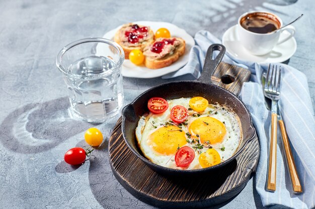 Uova fritte. Uova fritte da due uova in padella di ghisa con pomodorini e microgreens, pane tostato e tazza di caffè. Soleggiato concetto di colazione al mattino