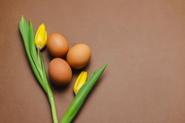 Uova marroni e tulipani gialli su un tavolo marrone. Tavola di Pasqua