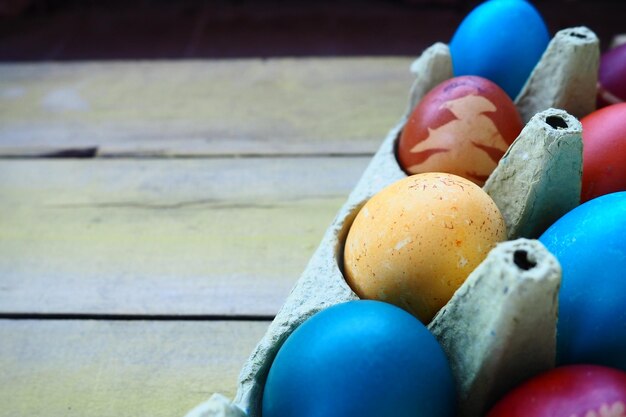 Uova multicolori dipinte con gouache e buccia di cipolla in una scatola di cartone su uno sfondo di tavolo in legno Dieci uova sode Cartoline poster per Pasqua Pasqua Uova rosse blu gialle marroni