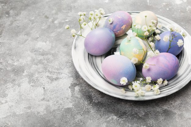 Uova multicolori per Pasqua in lastra di marmo con fiori bianchi su sfondo grigio. Copia spazio. Sfondo di cibo