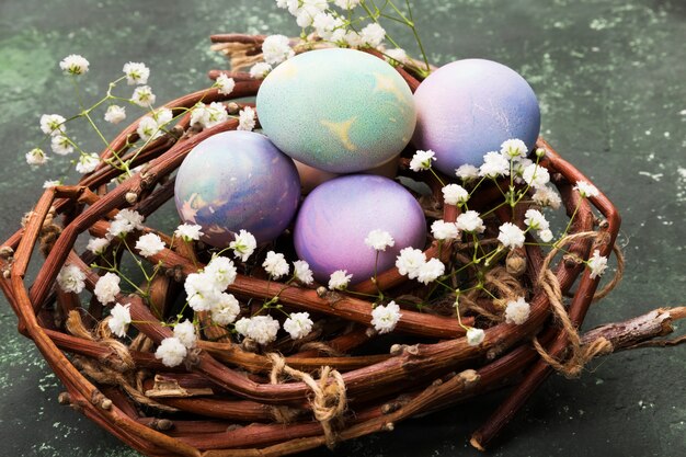 Uova multicolori per Pasqua in nido con i fiori su fondo verde