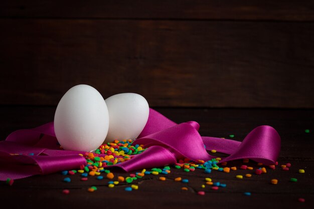 Uova, nastro rosa, dolci colorati sulla superficie in legno. Concetto di pasqua