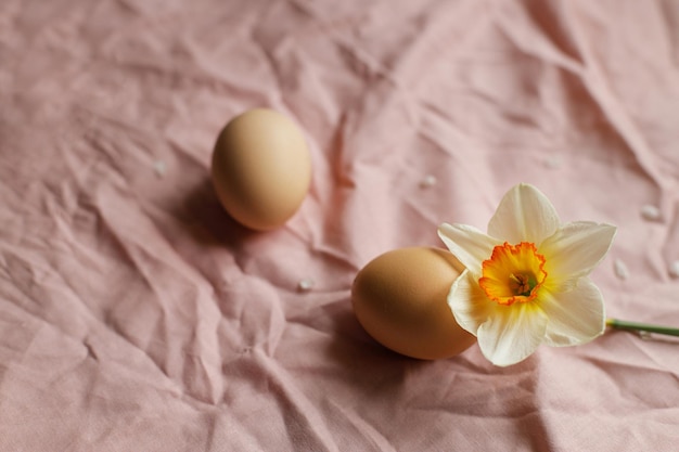 Uova naturali e fiore narciso in fiore su sfondo tessuto rosa Buona Pasqua Natura morta rustica di Pasqua Spazio per il testo