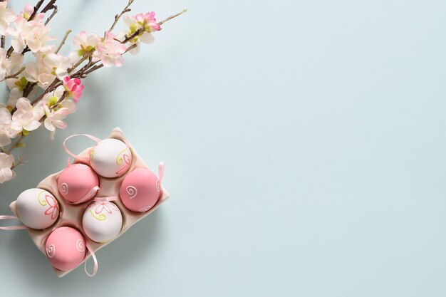 Uova pastello di Pasqua e fiori che sbocciano primaverili sull'azzurro.