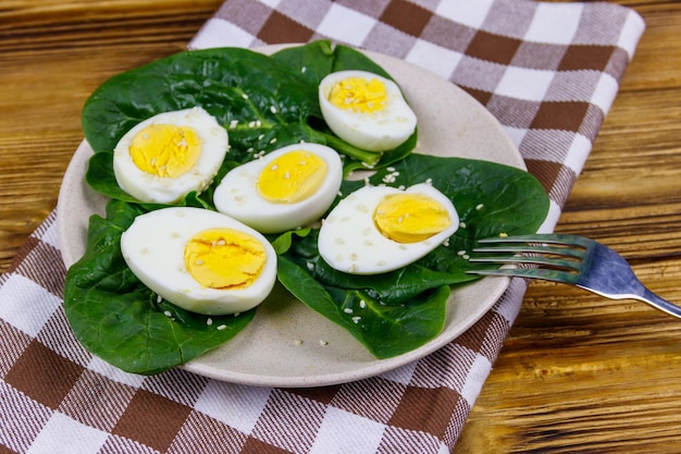 Uova sode con foglie di spinaci freschi e semi di sesamo sulla tavola di legno