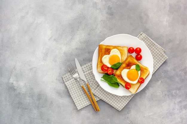 Uova strapazzate a forma di cuore sulla piastra con pomodori, verdure e caffè