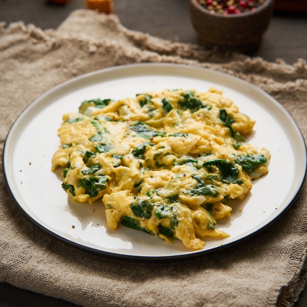 Uova strapazzate con spinaci, tazza di tè su sfondo marrone scuro.