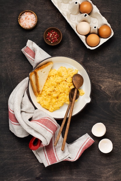 Uova strapazzate per colazione in padella, superficie del tavolo in legno scuro. Prima colazione inglese tradizionale. Vista dall'alto