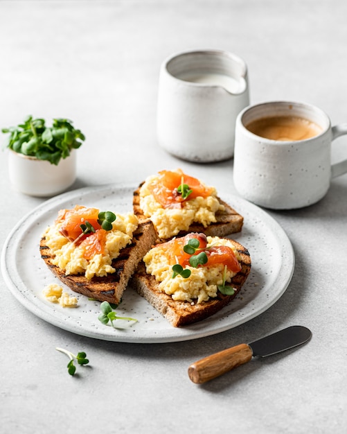 Uova strapazzate toast con salmone e microgreens su un piatto di ceramica bianca messa a fuoco selettiva