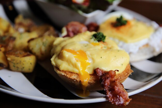 Uovo alla Benedict con pancetta e patate su fondo di legno