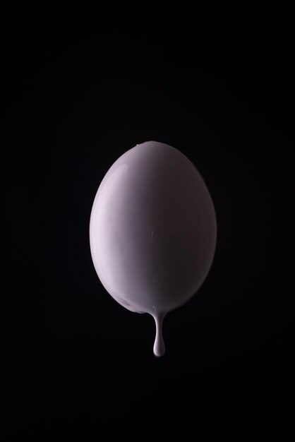 Uovo bianco che gocciola con gocce di vernice bianca su sfondo nero Concetto minimalista di pasqua