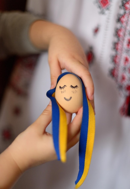 Uovo con faccia dipinta e nastro ucraino e ornamento ucraino su sfondo sfocato