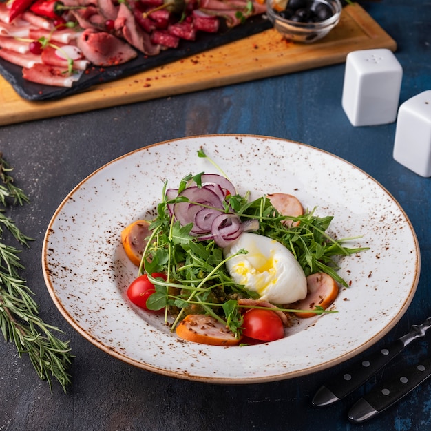 Uovo di Pashot, rucola, pomodorini e salsicce su un piatto. Uovo di pashot insalata sana e dieta.