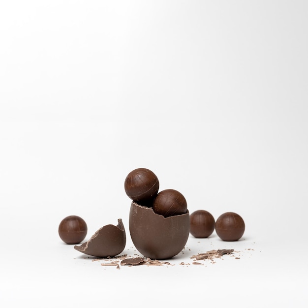 Uovo di Pasqua al cioccolato incrinato pieno di cioccolato piccole caramelle rotonde e cioccolatini su sfondo bianco spazio per la copia Delizia al cioccolato per i bambini Concetto di Pasqua