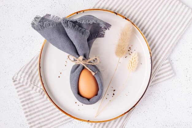 Uovo di Pasqua decorato come un coniglietto in un piatto bianco su uno sfondo di cemento bianco