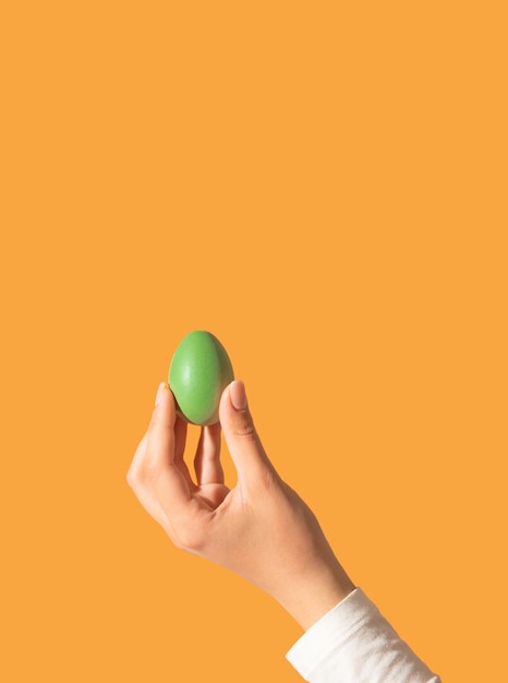 Uovo di Pasqua di colore verde in mano di una bella donna su sfondo arancione Stile estetico retrò