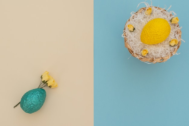 Uovo di Pasqua giallo colorato nel cestino dell'uovo con carta bianca come un nido e uovo blu con fiori primaverili gialli
