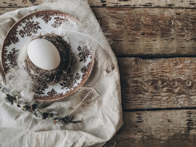 Uovo di Pasqua in nido di piume piatto d'epoca tovagliolo di lino rami di salice su tavola rustica