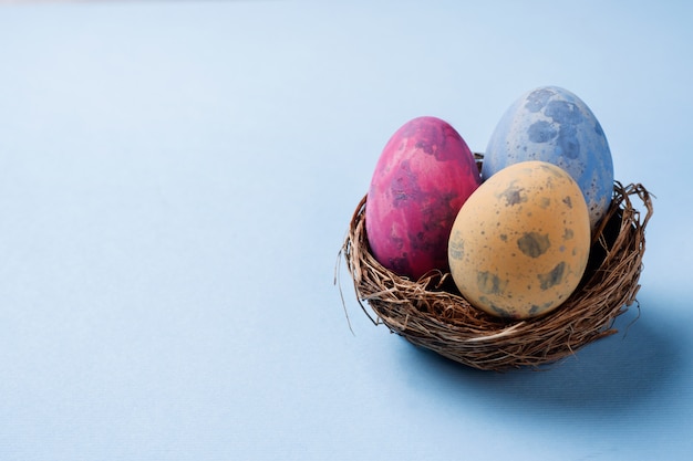 Uovo di Pasqua variopinto nel nido su fondo blu con lo spazio della copia. Sfondo di Pasqua minimalismo