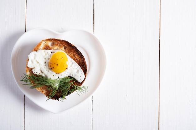 Uovo di quaglia fritto cotto in un panino rotondo su un piatto bianco a forma di cuore