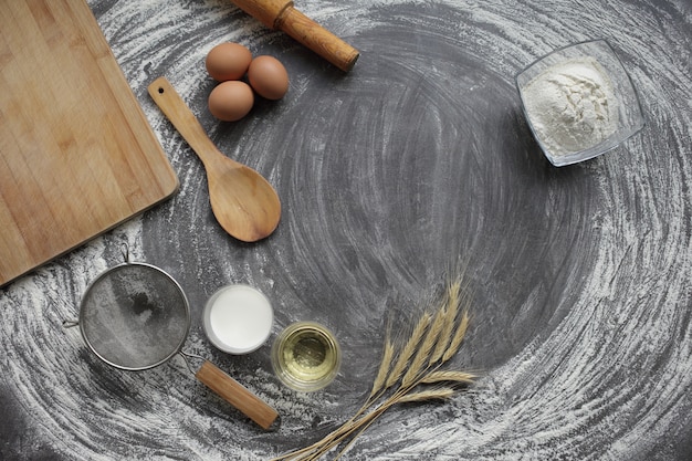 Uovo, farina, olio d'oliva, latte, spighe di grano, utensile da cucina su sfondo grigio tavolo.