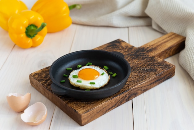 Uovo fritto con cipolle verdi in una padella di ghisa con peperoni su un tavolo di legno