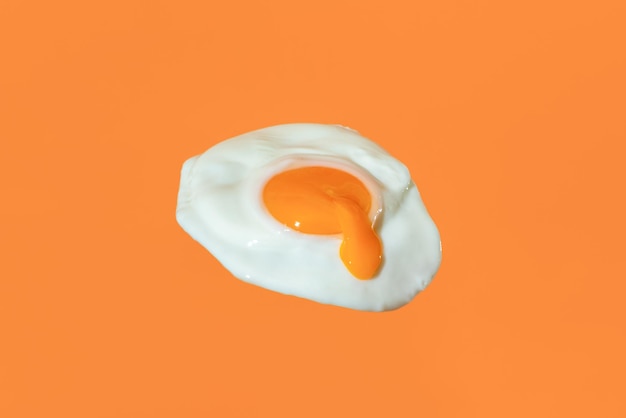 Uovo fritto minimalista su sfondo arancione con tuorlo d'uovo gocciolante