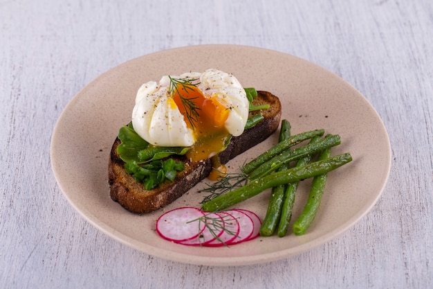 Uovo in camicia su un pezzo di pane con fagiolini fritti, ravanello e rucola su un piatto