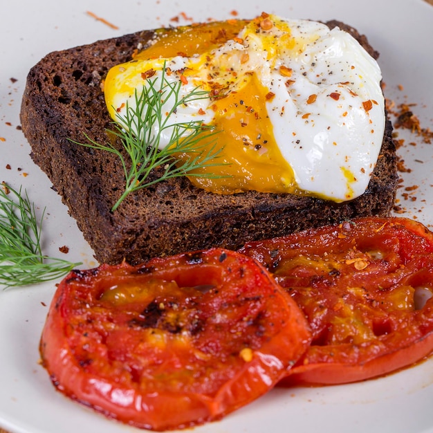 Uovo in camicia su un pezzo di pane con pomodori rossi fritti da vicino