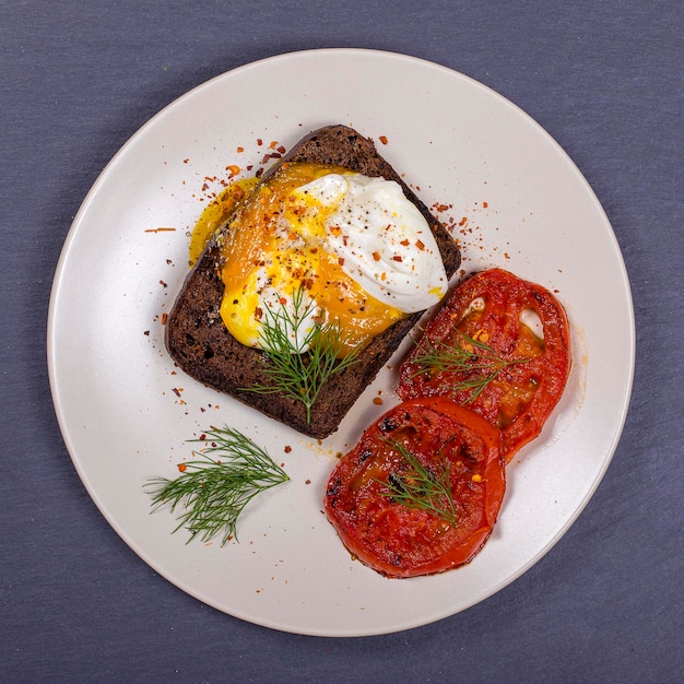 Uovo in camicia su un pezzo di pane con pomodori rossi fritti primo piano vista dall'alto