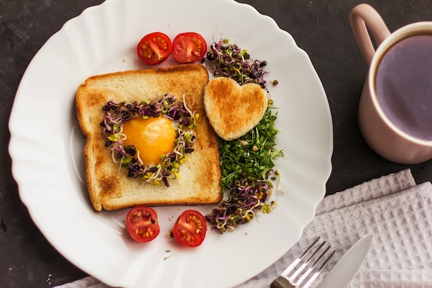 Uovo in un buco di pane a forma di cuore, microgreens, cibo sano Colazione, tè, sfondo nero