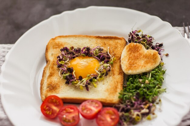 Uovo in un buco di pane a forma di cuore, microgreens, cibo sano Colazione, tè, sfondo nero