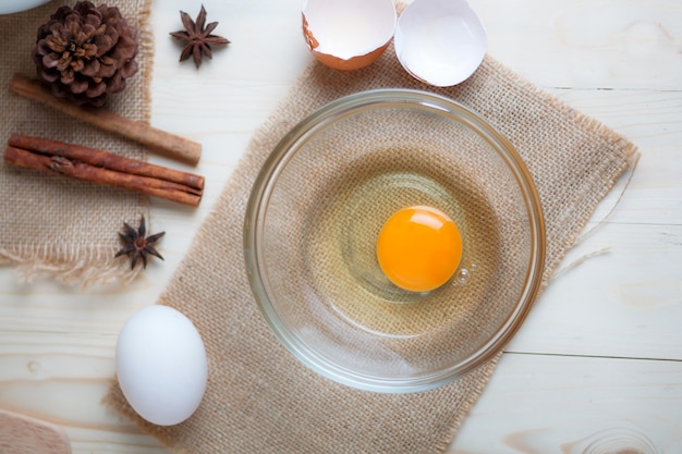 Uovo sulla ciotola di vetro chiaro sul tagliere di legno con ingredienti da forno
