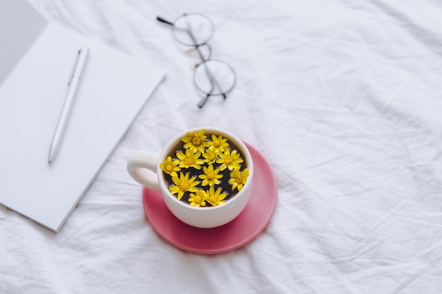 Ðup con fiori gialli all'interno, su un letto bianco con blocco note e penna.