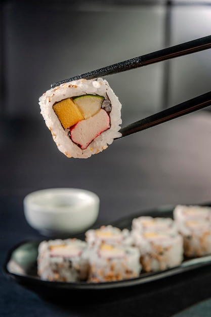 Uramaki con cetriolo, mango e bastoncini di granchio sulle bacchette. Avvicinamento.