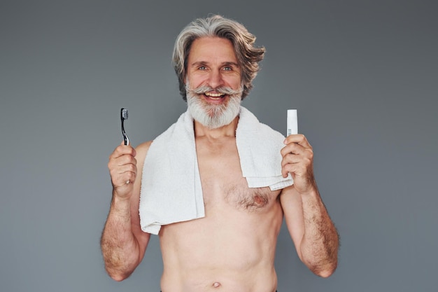 Usando il dentifricio L'uomo anziano moderno ed elegante con i capelli grigi e la barba è al chiuso