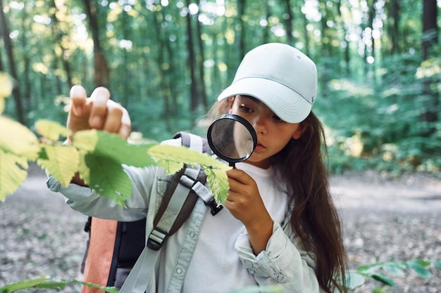 Usando la lente d'ingrandimento La ragazza è nella foresta durante il giorno d'estate alla scoperta di nuovi posti