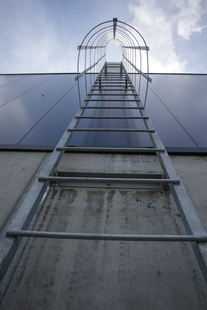 Uscita antincendio sull'edificio industriale sopra, vista dal basso. Corrimano in acciaio inox, scala da tetto. Vista di dettaglio delle scale con gabbia di sicurezza. Concetto di costruzione di edifici.