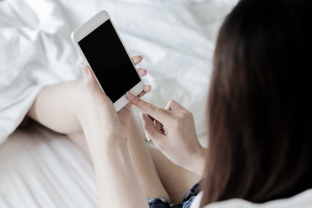 uso asiatico sexy della donna dello smartphone sul letto, scarsa visibilità