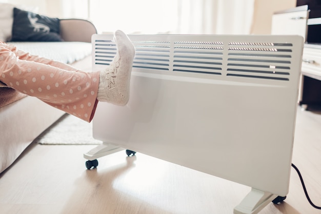 Uso del riscaldamento a casa in inverno. Donna che scalda i suoi piedi. Stagione di riscaldamento.