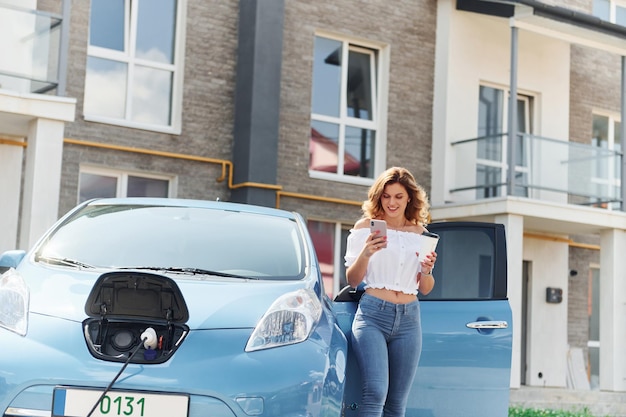 Uso del telefono Giovane donna in abiti casual con il suo elettromobile all'aperto durante il giorno