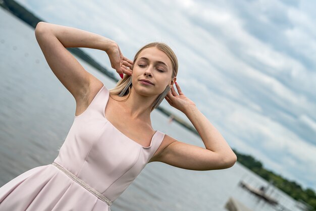 Usura abbastanza giovane della donna in vestito da sera rosa di modo che posa vicino al lago nel parco. Stile di vita