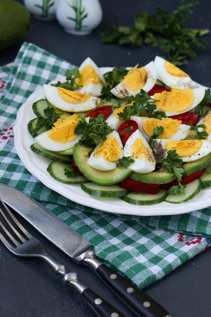 Utile insalata di avocado, cetrioli, uova e peperone dolce situata in un piatto su una superficie scura